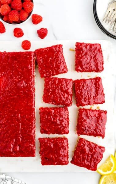 raspberry shortbreads cut into squares on a cutting board next to lemons and strawberries