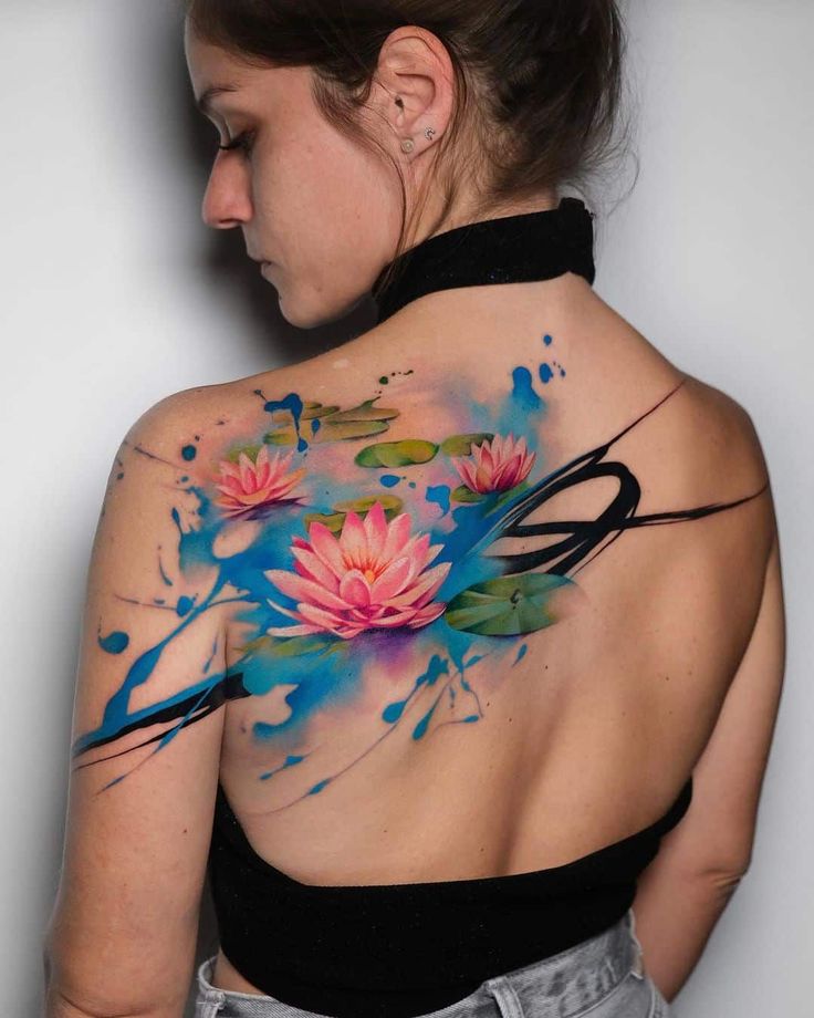 a woman's back tattoo with water lilies and blue paint splatters