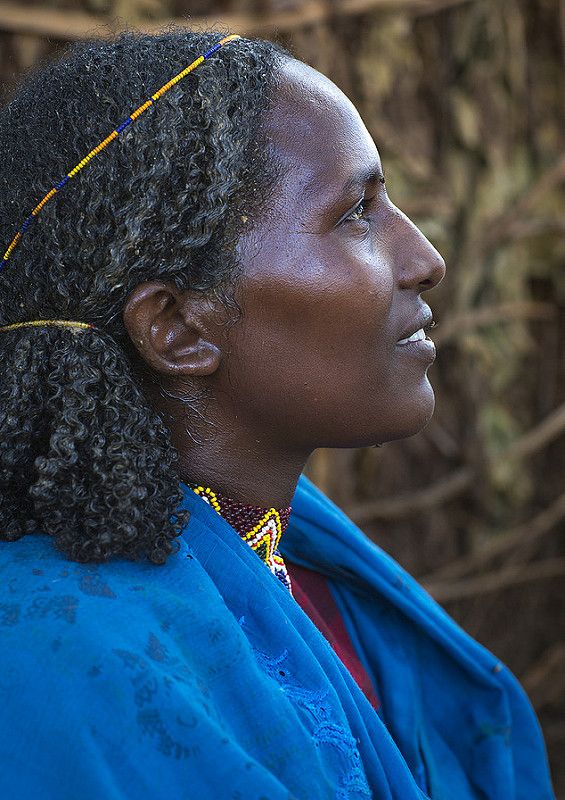 a woman with braids and blue jacket looking off into the distance in front of trees