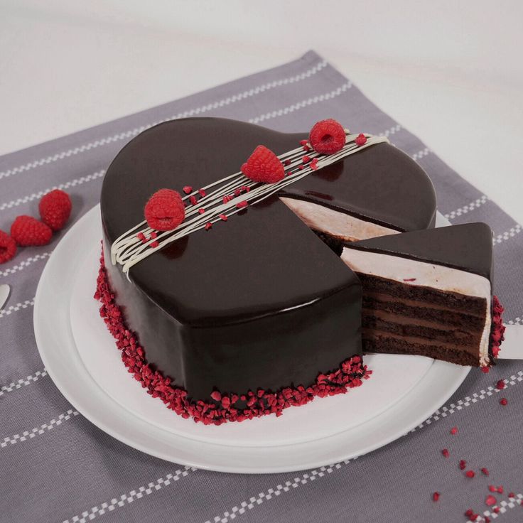 a heart shaped chocolate cake with raspberries on the top and one slice cut out