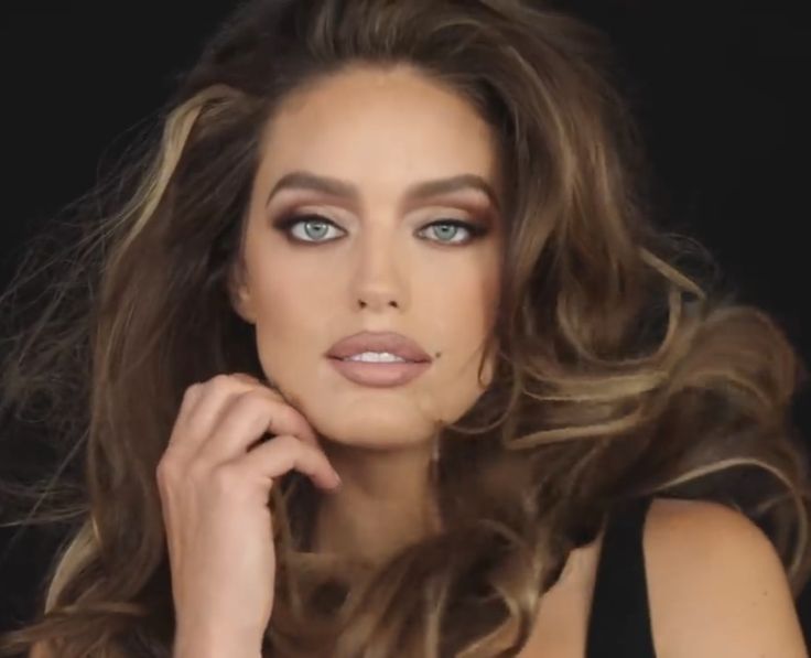 a woman with long brown hair and blue eyes posing for a photo in front of a black background