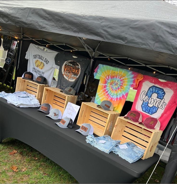 an outdoor market with t - shirts and other items on display under a tented area