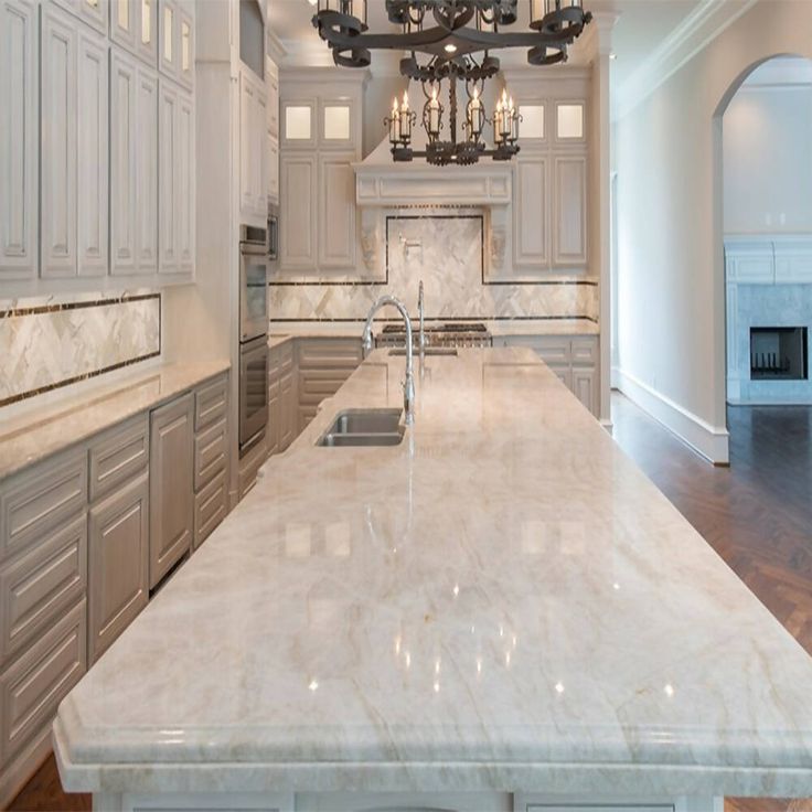 a large kitchen with marble counter tops and white cabinets, chandelier hanging from the ceiling