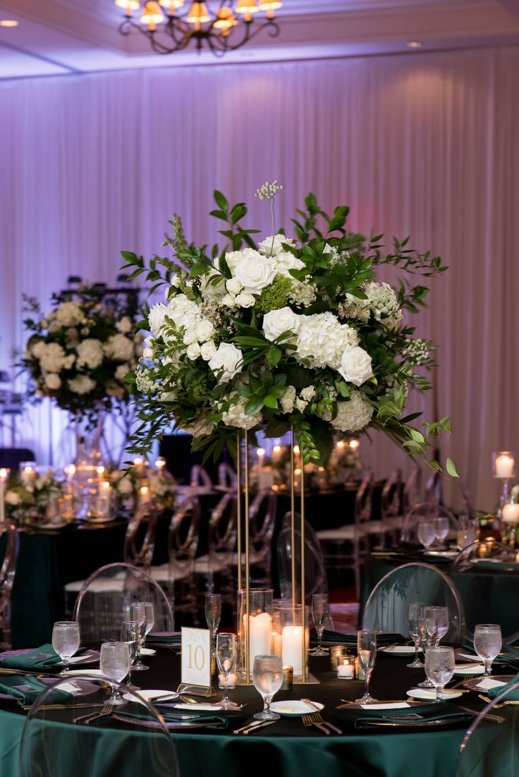 a tall vase with white flowers and greenery sits on top of a round table