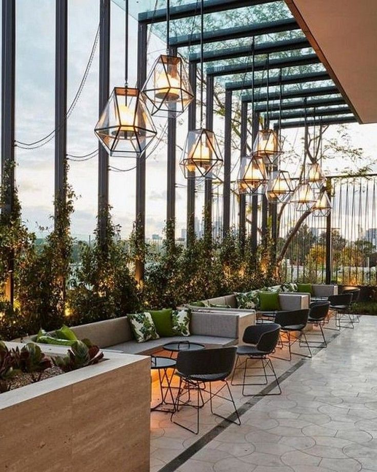 an outdoor seating area with lots of plants and lights hanging from the ceiling above it