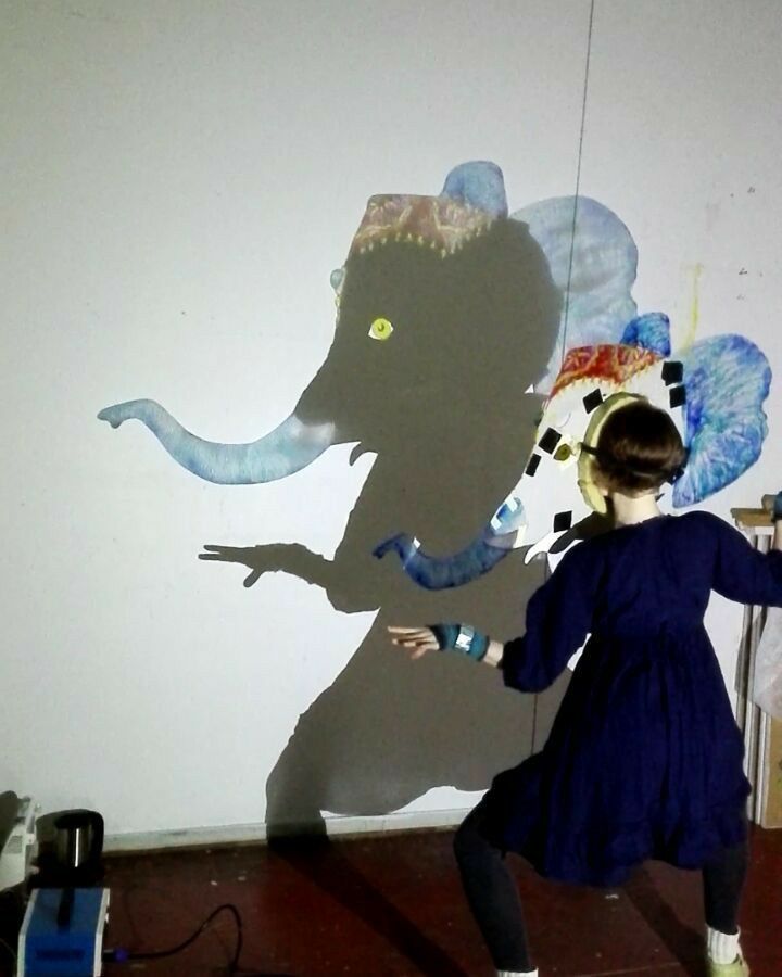 a woman standing in front of a giant shadow of an elephant