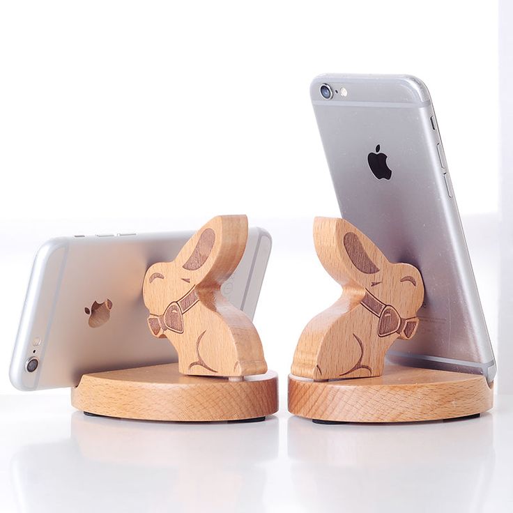 the wooden phone stand is holding an iphone and a small rabbit figurine on it