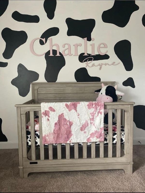 a baby crib in front of a cow print wall with the name charlie on it