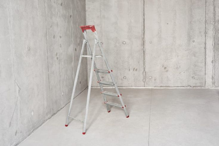 a ladder leaning against a wall in an unfinished room with concrete walls and red paint