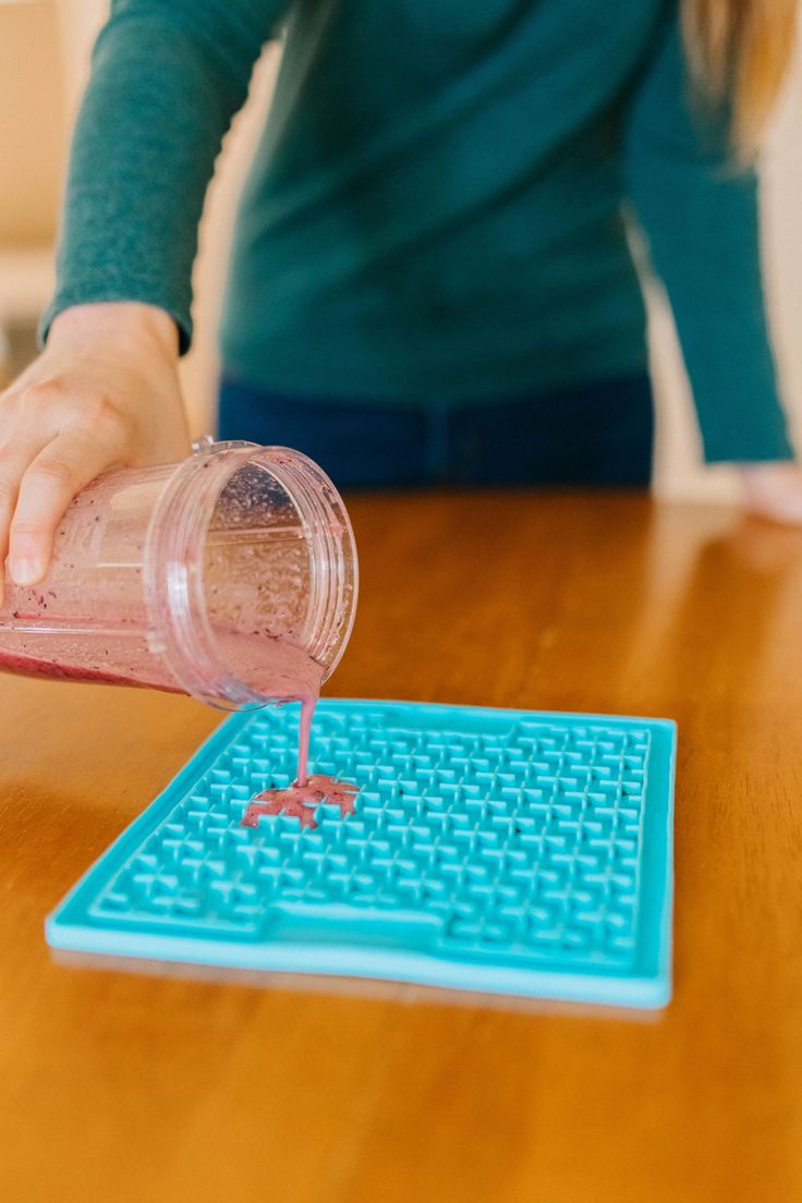 a person pouring something into a cup on top of a wooden table with the words prevent bored dogs with a lickmat