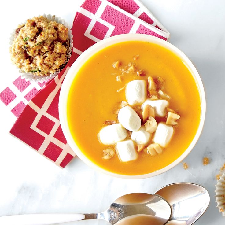 there is a bowl of soup with marshmallows in it and two spoons next to it