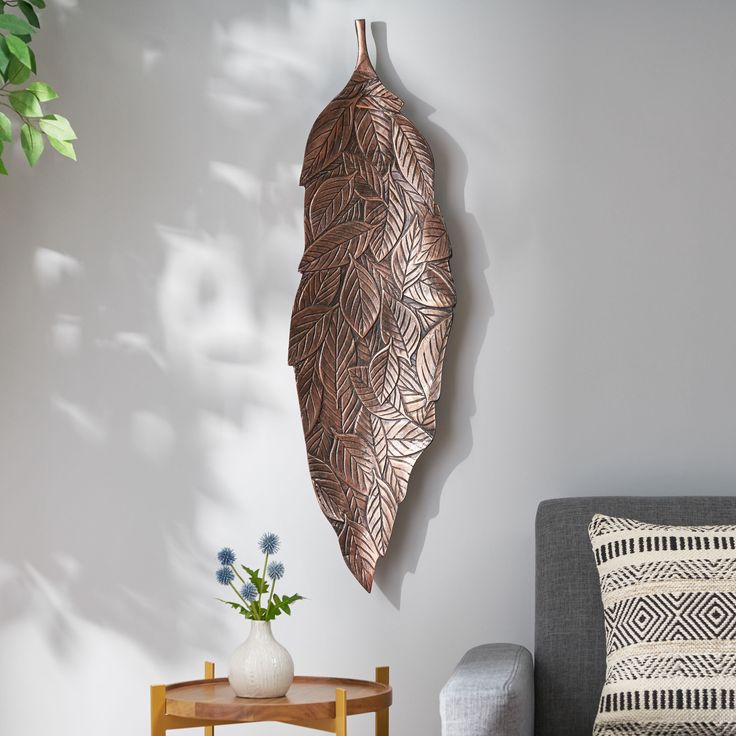 a metal leaf hanging on the wall next to a table with flowers and a vase