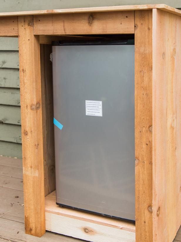 a small refrigerator sitting on top of a wooden table next to a building with siding