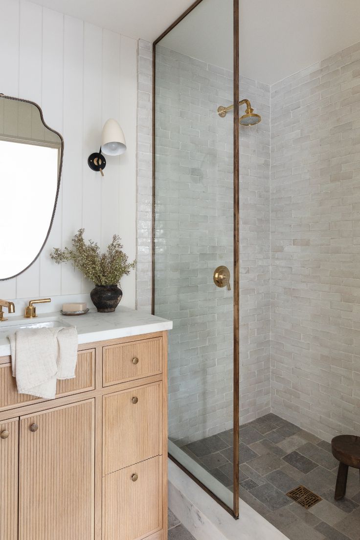 a bathroom with a walk in shower next to a white sink and wooden cabinetry