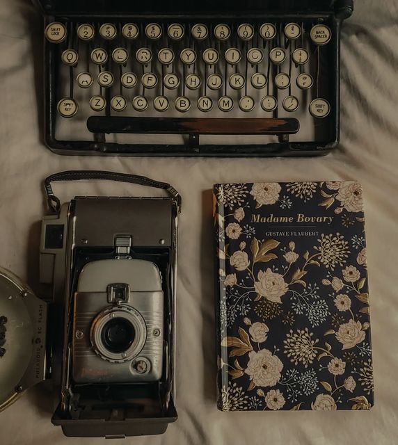 an old fashioned typewriter, camera and book on a white bed with floral sheets