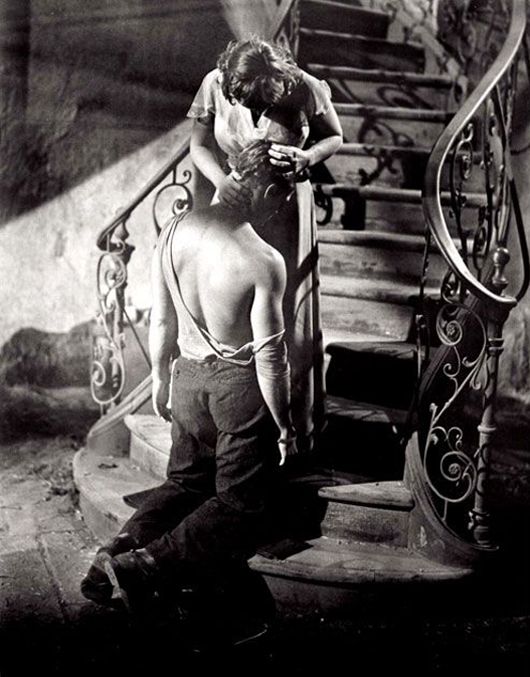 an old photo of two men on the stairs with their backs to each other and one man holding something in his hand