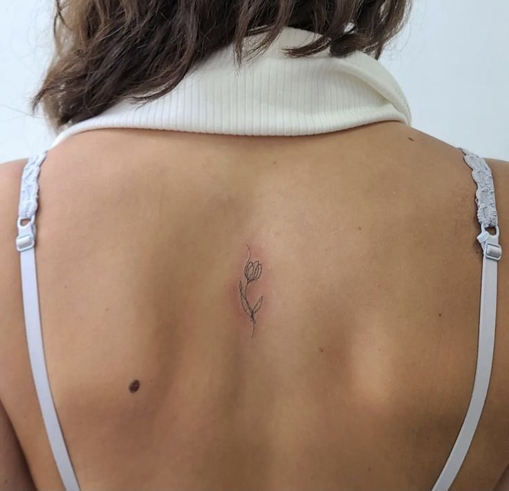 a woman's back with a small flower tattoo on her left side ribcage