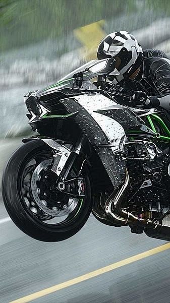 a man riding on the back of a black and green motorcycle down a street next to trees