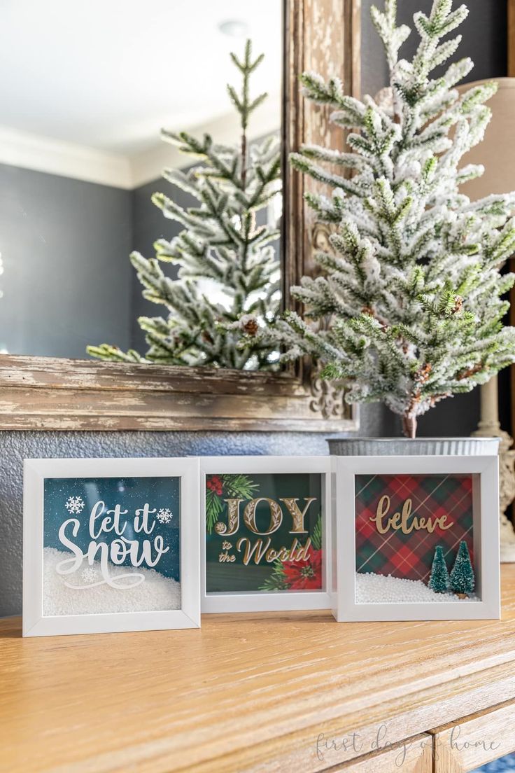 three christmas cards sitting on top of a wooden table next to a small pine tree