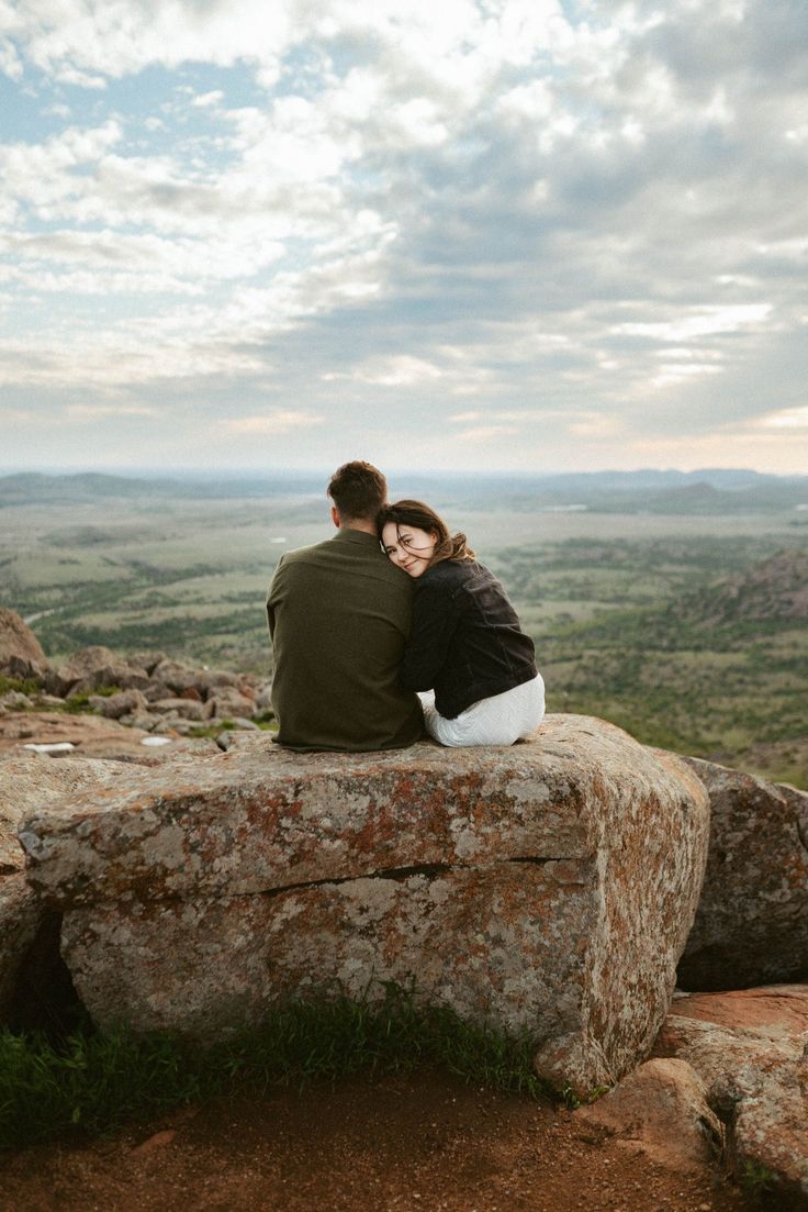 a man and woman sitting on top of a large rock in the middle of nowhere