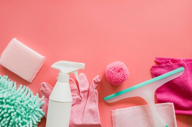 various household cleaning supplies laid out on a pink background, including gloves and sponges