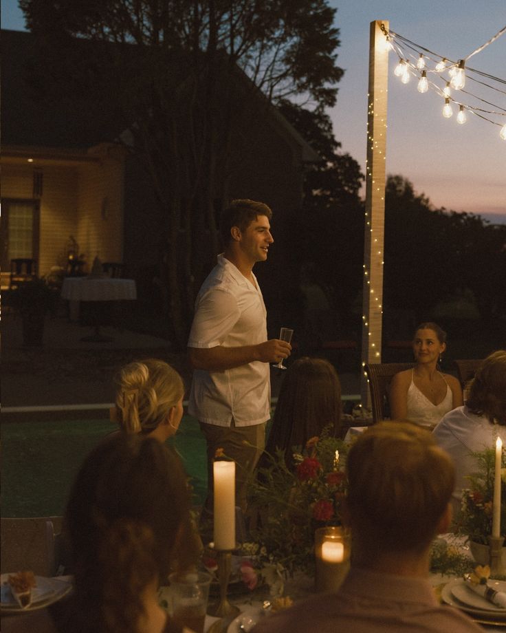 a man standing in front of a group of people at a dinner table with lit candles