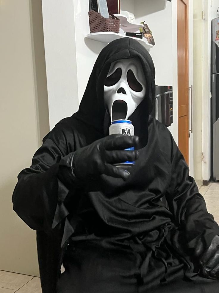 a person in a ghost costume sitting down with a cell phone to their ear and mouth