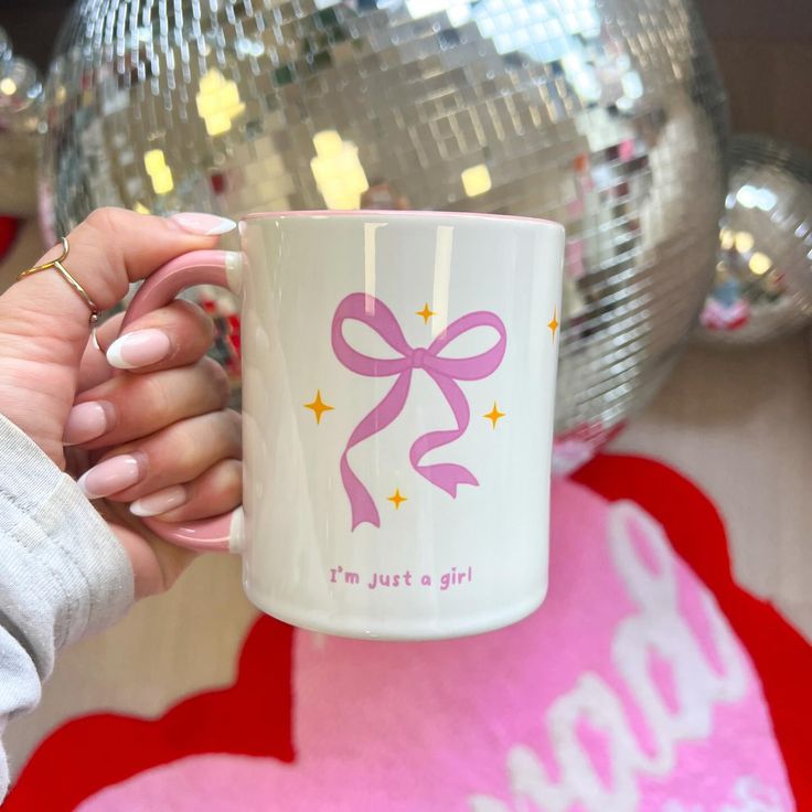 a woman holding a coffee mug with a pink bow on it's handle and the words i'm just a girl