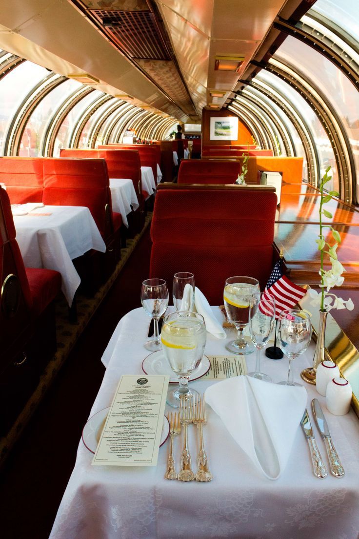 a dining car on a train with white tablecloths and silverware set for two