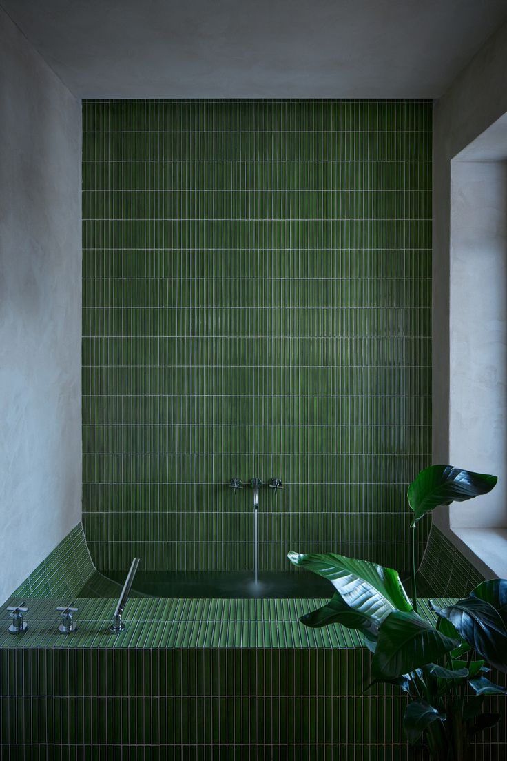 a green tiled bathroom with a plant in the bathtub and shower faucet