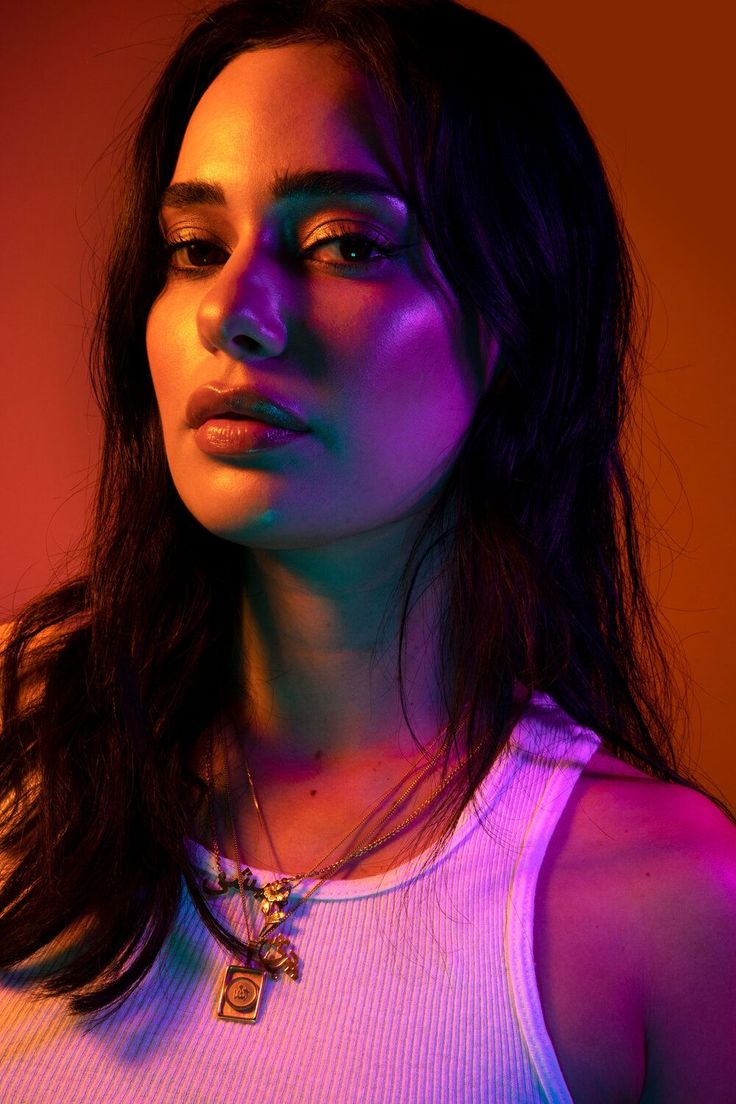 a woman with long hair wearing a white tank top and colorful lights on her face