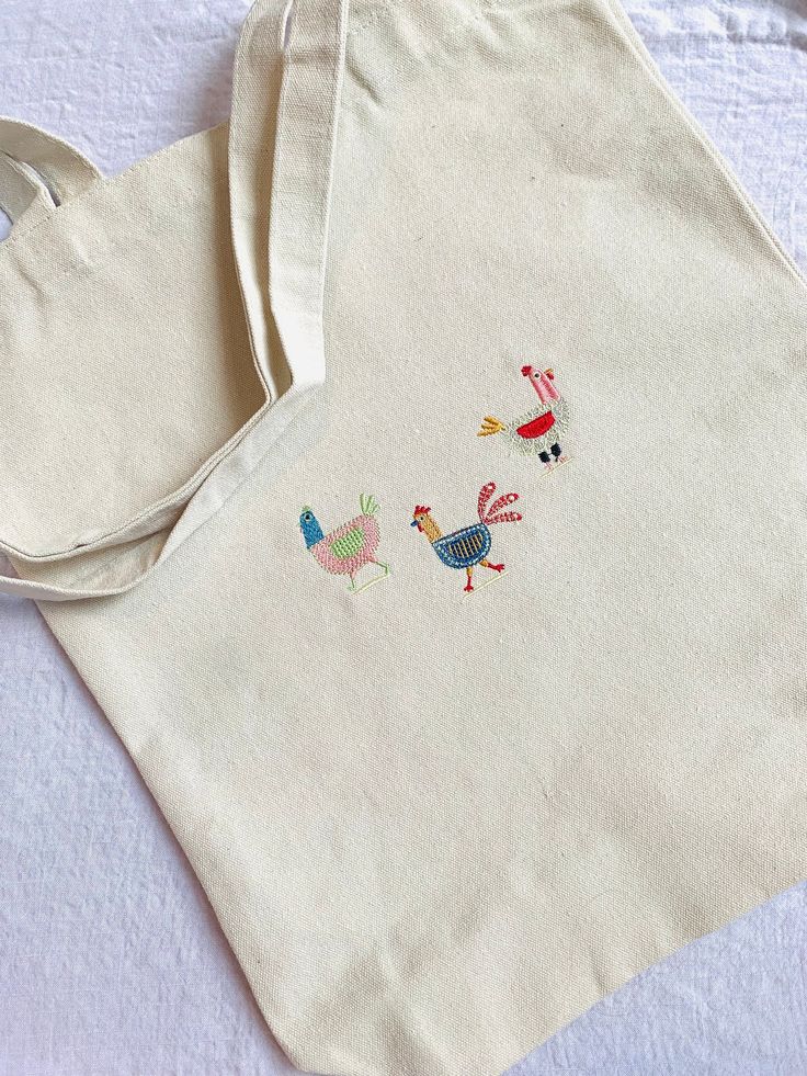 an embroidered tote bag sitting on top of a white tablecloth covered table cloth