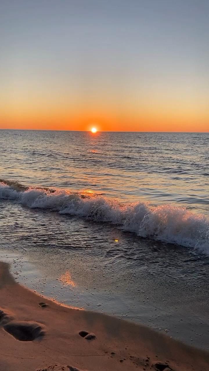 the sun is setting over the ocean with waves crashing on the beach and footprints in the sand