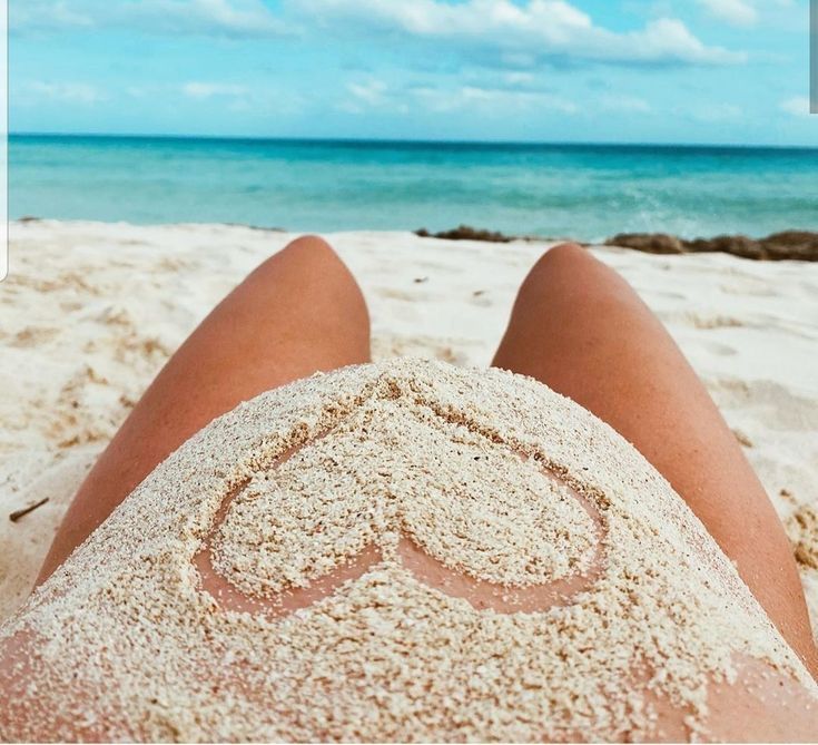 a person laying in the sand with their legs crossed and heart drawn on it's back