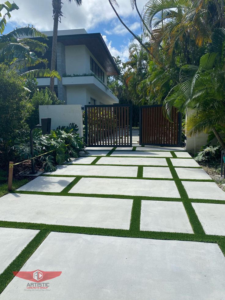 an outdoor walkway with artificial grass in front of a white house and palm trees on the other side