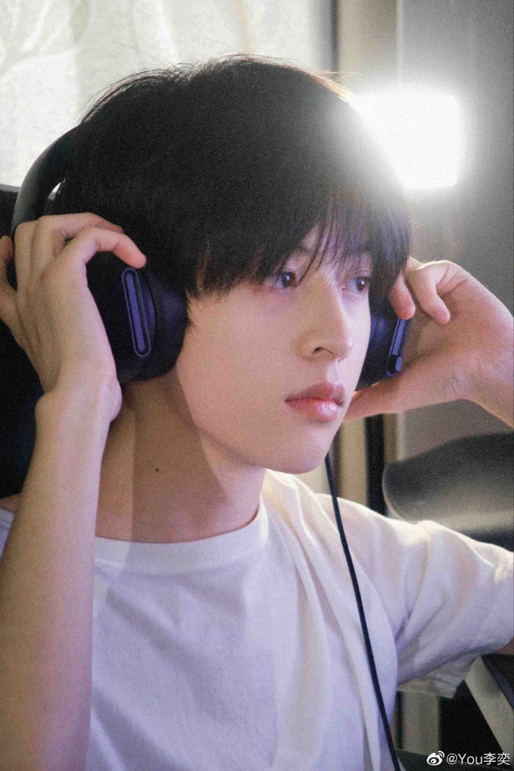 a young man listening to music with headphones on his ears and holding a cell phone up to his ear