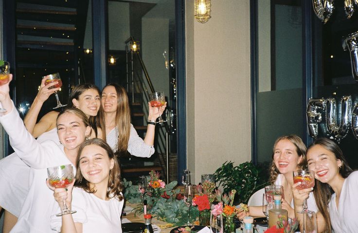 a group of women sitting at a table with drinks in front of them and smiling