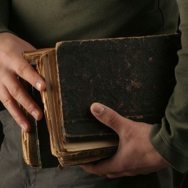 a person holding an old book in their hands with both hands on the open cover