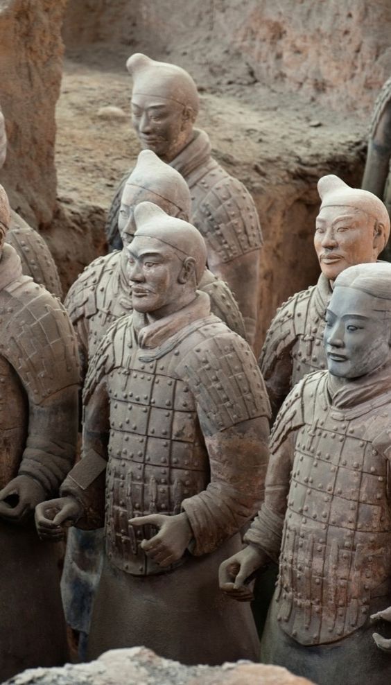 a group of statues of men in armor standing next to each other on dirt ground