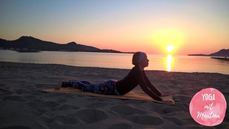 a woman laying on top of a sandy beach next to the ocean at sunset with a yoga mat in front of her