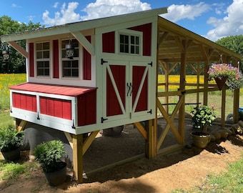 a small red and white chicken house in the middle of a field with yellow flowers