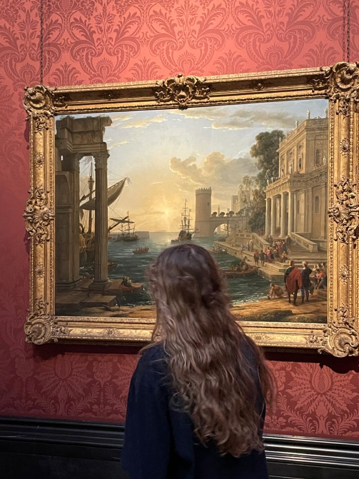 a woman standing in front of a painting on display at an art museum, looking at it