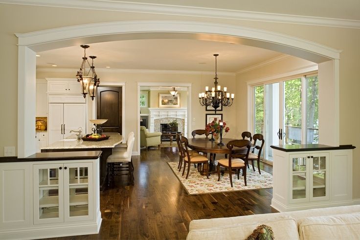 a large open concept kitchen and dining room with hardwood floors, white cabinets, an arched doorway leading to the living room