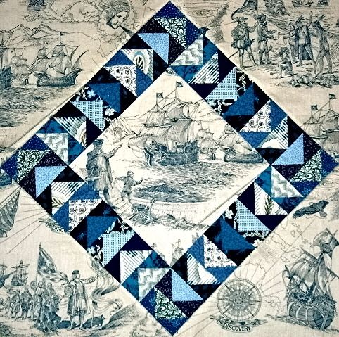 a blue and white quilt with an image of people on boats in the water below it