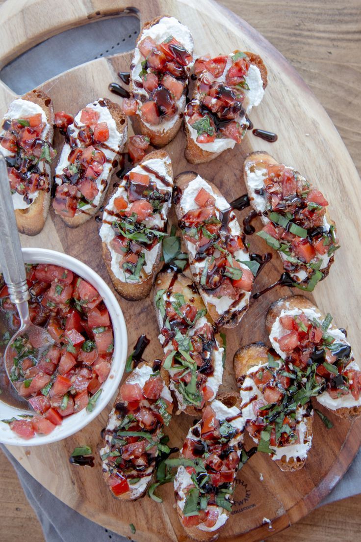 a wooden platter topped with mini sandwiches covered in toppings and garnish