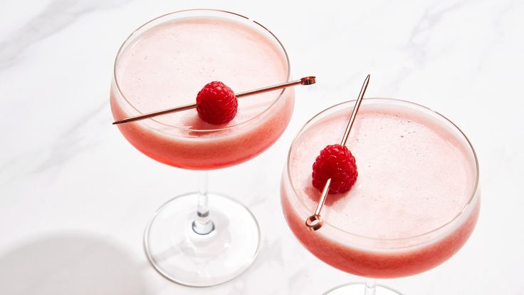 two glasses filled with raspberry martinis sitting on a counter top next to each other