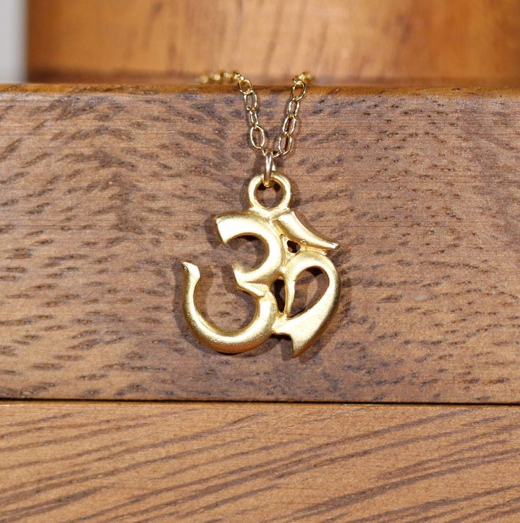 "Ohm necklace, spiritual necklace, gold ohm pendant, yoga necklace, peace necklace, a 14k gold vermeil ohm on a 14k gold filled chain A 14k gold vermeil ohm symbol hangs peacefully from a 14k gold filled chain in the length of your choice! This ohm pendant measures 13mm. Ohm is a holy meditation symbol of Hinduism, Buddhism, and Jainism with a profusion of esoteric and exoteric meanings. In modern usage Om means the Word, the \"parnava,\" the eternal. Need a pop of color? You can add a little to Ohm Necklace, Meditation Symbols, Necklace Spiritual, Ohm Pendant, Ohm Symbol, Spiritual Necklace, Peace Necklace, Yoga Necklace, Gold Filled Chain