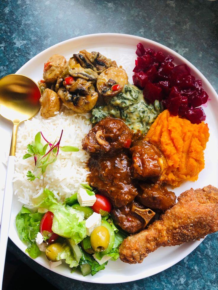 a white plate topped with meat, rice and veggies next to a spoon