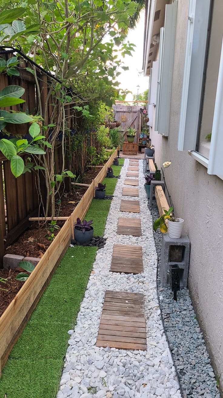 a long narrow garden lined with gravel and wooden benches next to a fenced in yard