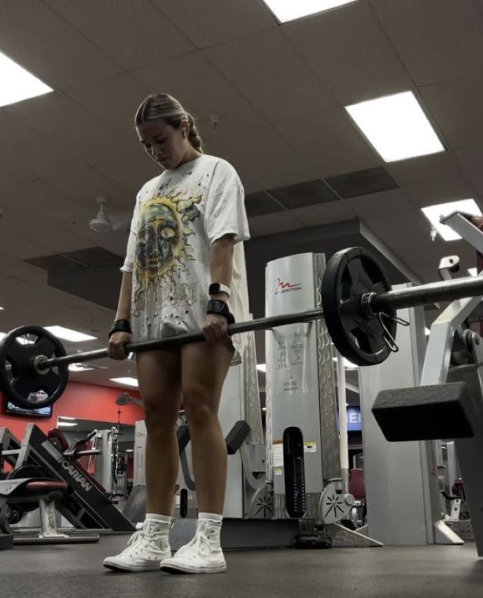 a woman standing in the middle of a gym holding a barbell